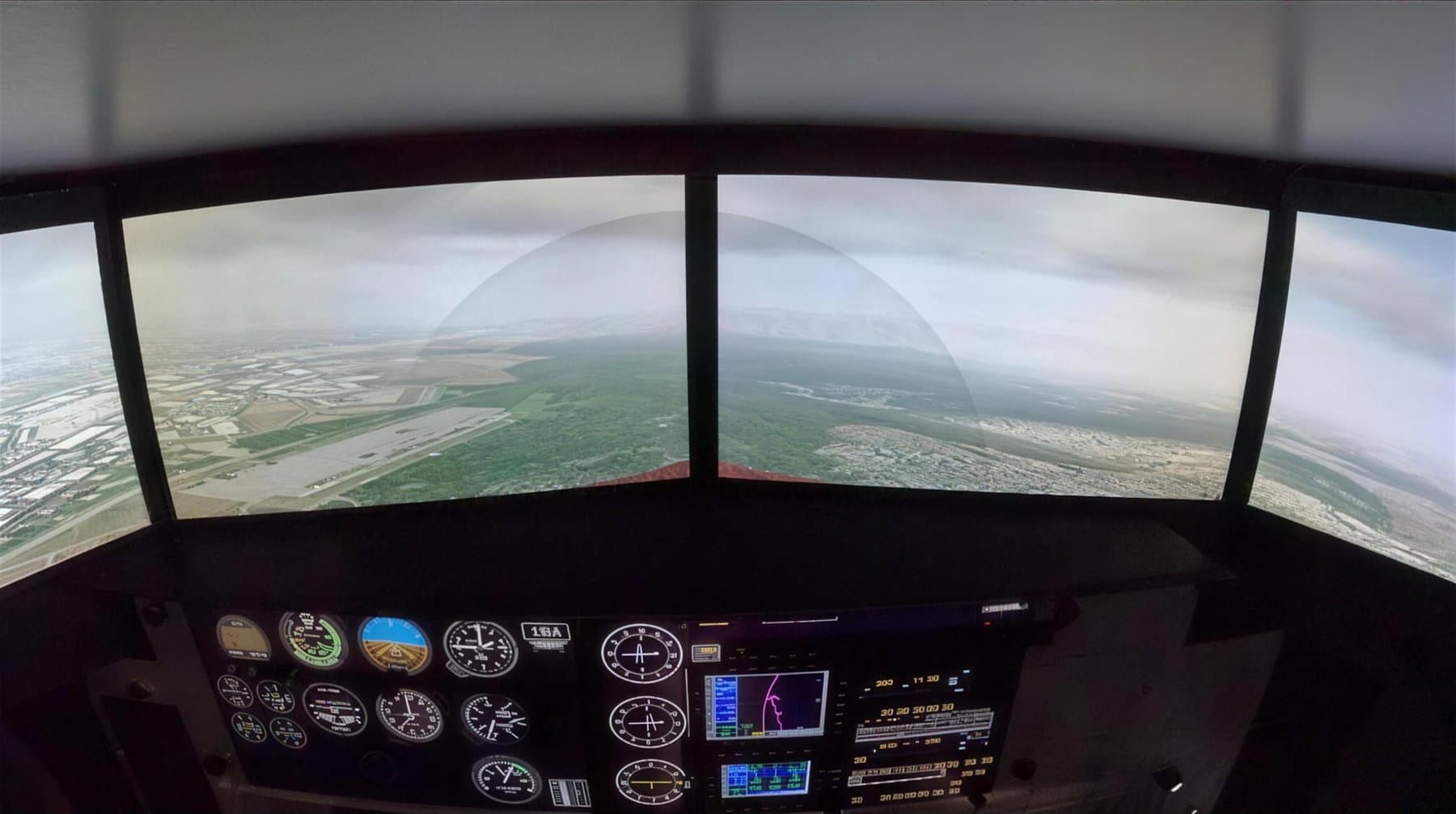 Instrument panel and wraparound visuals inside the Redbird FMX simulator on approach to a runway